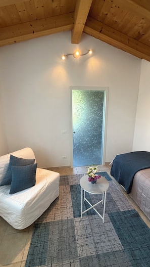 A cozy room with a bed, a small table with a vase, and a window with frosted glass. - Pool & Garden Small House (Veneto)