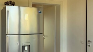 Een koelkast van roestvrij staal in een kamer met een witte tafelkleed, een schaal met fruit en een bloevas.