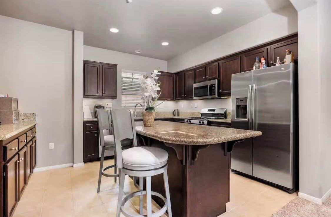 A modern kitchen with dark wood cabinets, stainless steel appliances, and a granite countertop island with two bar stools.