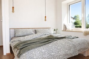 Ein Schlafzimmer mit einem Bett, einem Fenster mit Blick und einem Nachttisch mit einer Vase.