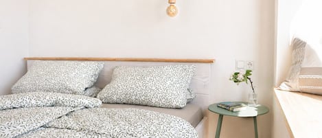 Ein Schlafzimmer mit Bett, Kissen, Nachttisch, Lampe und einer Steckdose.