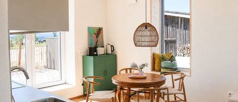 A compact kitchen with a sink, a dining area with a round table and chairs, a green cabinet, and a window with a view of the outside.