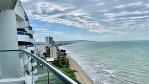 A balcony with a view of a beach and ocean, a modern building with multiple floors, and a clear sky. - Grand Diamond Beach, Luxury Oceanfront Suite🌟 (Tonsupa)