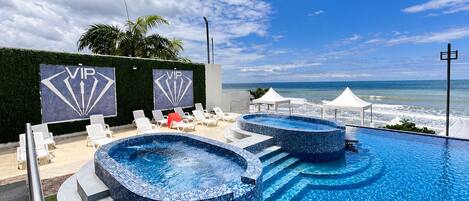A pool area with lounge chairs and a hot tub, a VIP sign, and a view of the ocean.