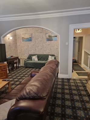 A living room with a brown leather sofa, a green sofa, a wooden table, and a patterned carpet.