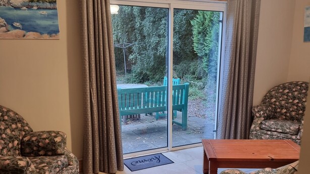 Un salon avec un canapé, une table basse et une vue sur un jardin, accessible par une porte-fenêtre coulissante.