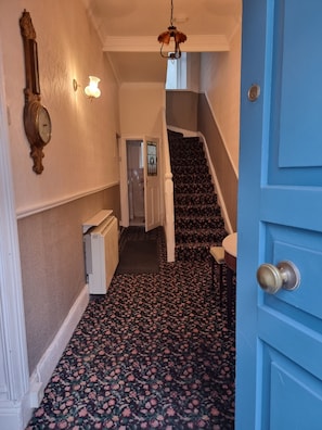 A hallway with a patterned carpet, a clock, a wall-mounted light fixture, and a blue door.
