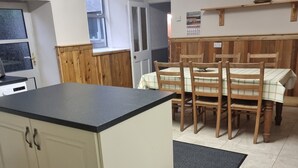 Une cuisine dotée d’un îlot central, de chaises en bois et d’une table à manger recouverte d’une nappe à carreaux.