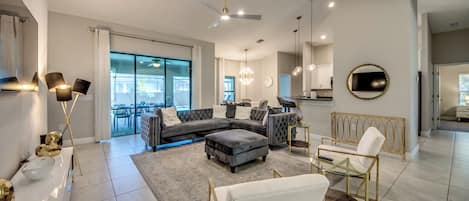 A modern living room with a sectional sofa, ottoman, glass coffee table, and a dining area with a white chair and gold accents.