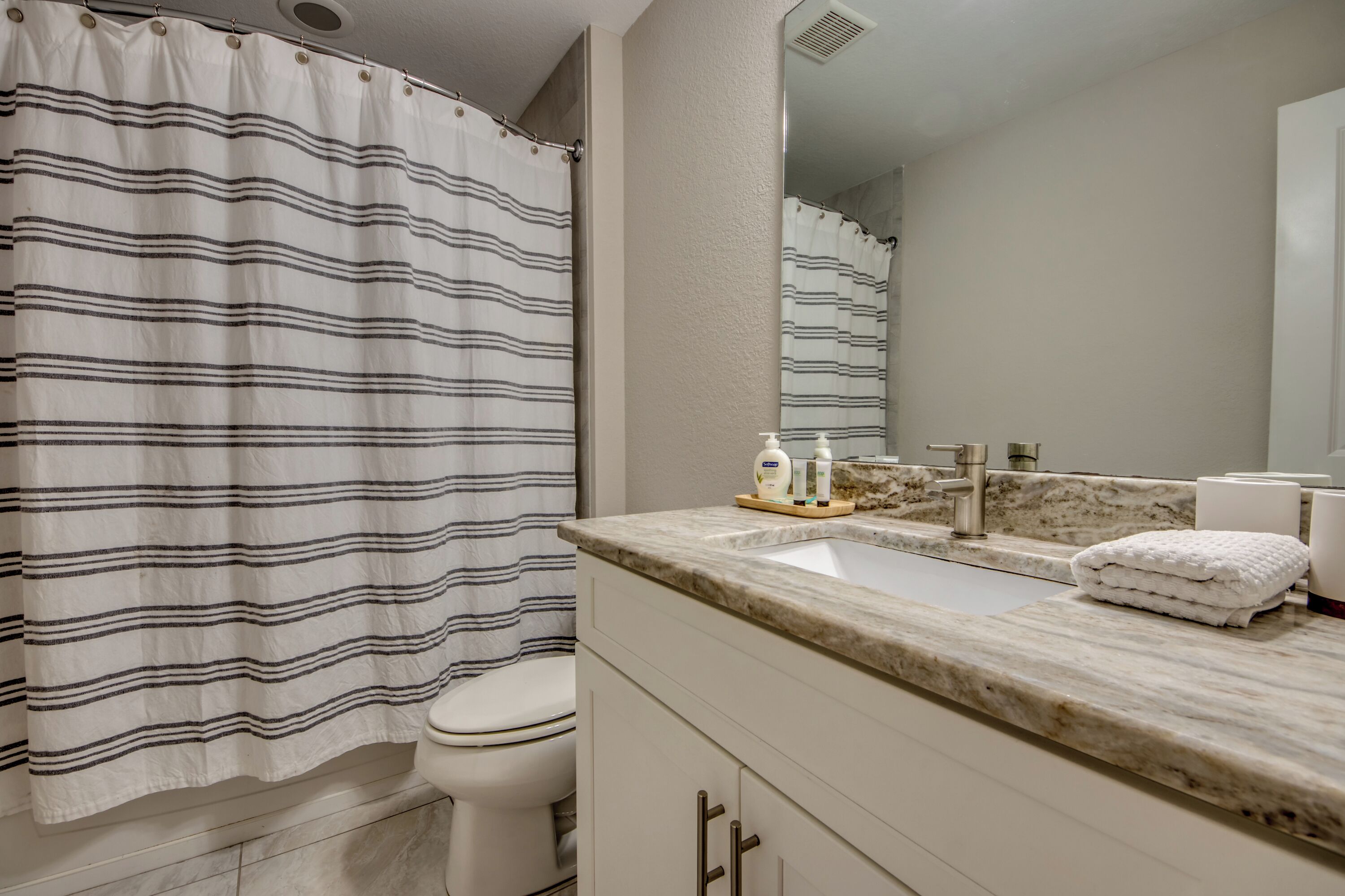 A bathroom with a striped shower curtain, a sink with a marble countertop, and a mirror reflecting the shower area.