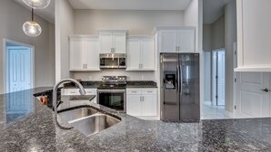 A modern kitchen with white cabinets, stainless steel appliances, granite countertops, and pendant lighting. - Luxury Cape Coral Oasis: Pool, Sleeps 8 (Cape Coral)