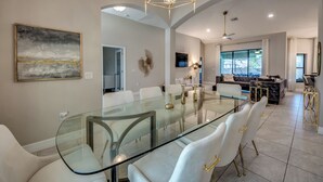 A modern dining area with a glass table, white chairs, and a geometric chandelier. - Luxury Cape Coral Oasis: Pool, Sleeps 8 (Cape Coral)