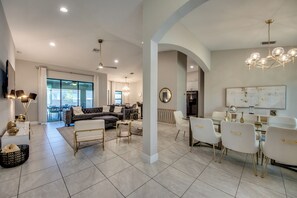 A spacious living area with a modern sofa, dining table, and chairs, a chandelier, and a large window providing natural light. - Luxury Cape Coral Oasis: Pool, Sleeps 8 (Cape Coral)