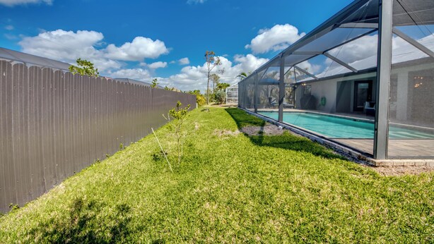 A backyard with a swimming pool, a covered patio area, and a wooden fence. - Luxury Cape Coral Oasis: Pool, Sleeps 8 (Cape Coral)