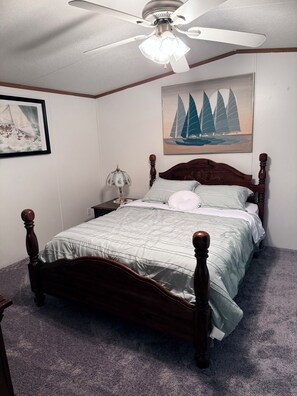 A bedroom with a wooden bed, a ceiling fan, a nightstand, a lamp, and two framed pictures on the wall. - 5 Peaceful Acres•Pet Friendly•Short Drive to Beach (Milton)