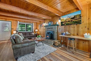 A cozy cabin interior with a fireplace, wooden walls, a sofa, and a bar area. - Mtn Retreat Hot Tub~Lake 20 min (Mi-Wuk Village)