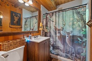 Un bagno con tenda da doccia a tema cervo, pareti in legno, un lavandino e uno specchio.