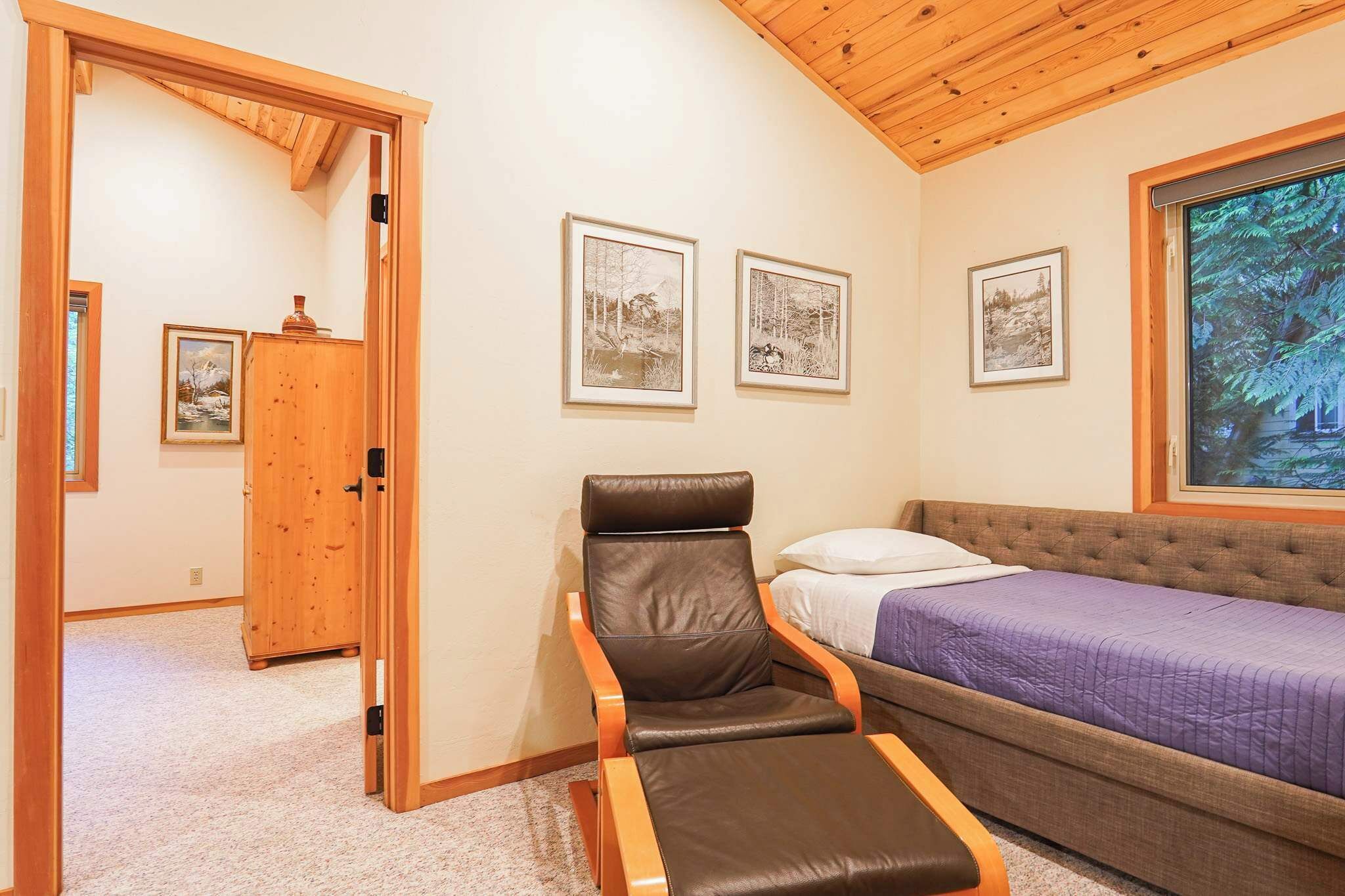 A bedroom with a bed, a reclining chair, and framed pictures on the wall.