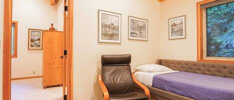 A bedroom with a bed, a reclining chair, and framed pictures on the wall.