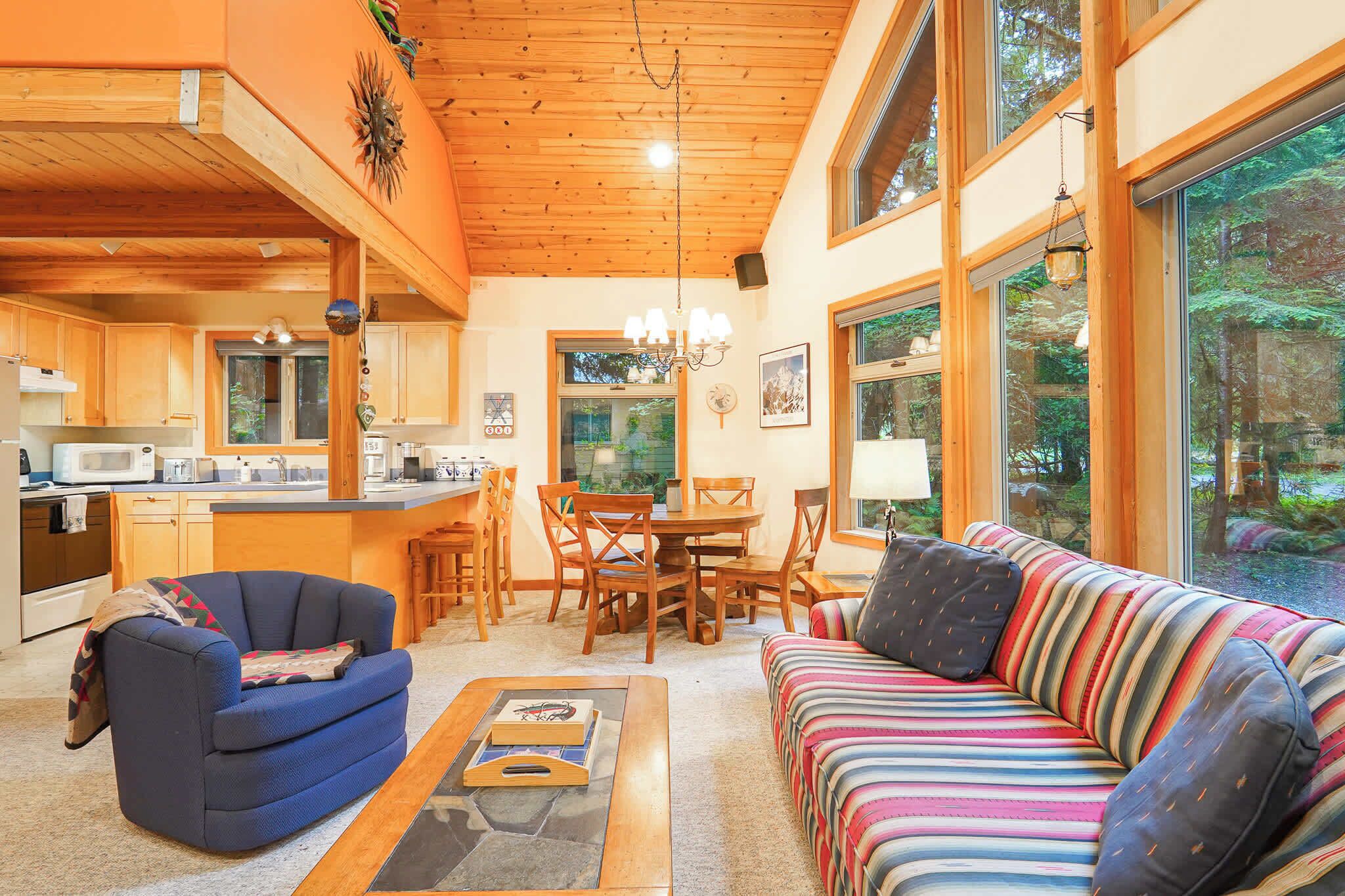 Un intérieur chaleureux avec un coin repas, un plafond en bois, de grandes fenêtres et un canapé à rayures.
