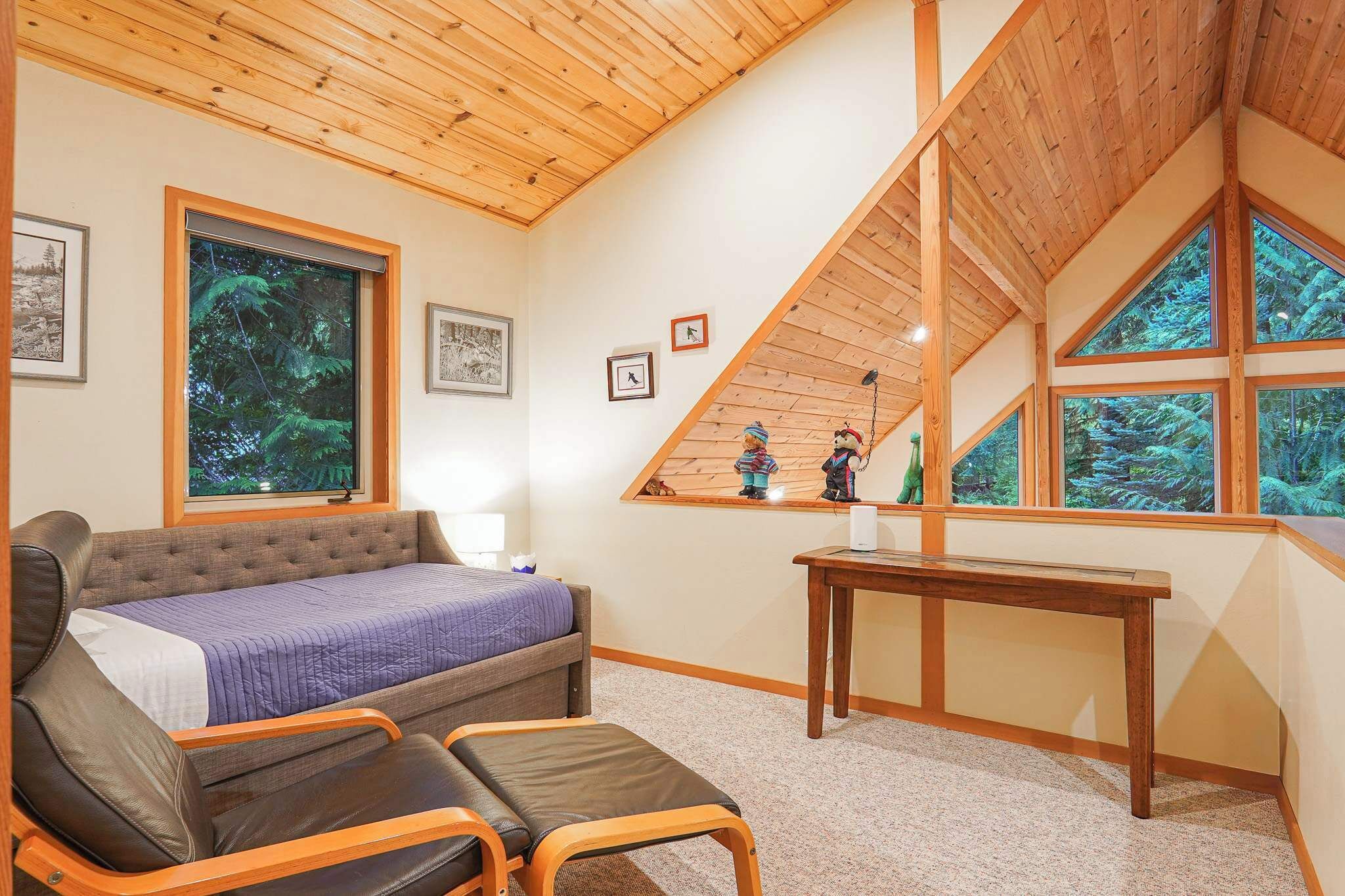 Ein Schlafzimmer mit einem Bett, einer Bank, einem Tisch und großen Fenstern mit Blick auf Bäume.