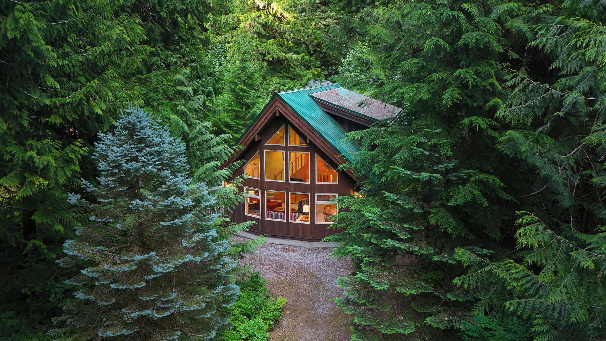 Eine Hütte, umgeben von dichtem Wald, mit einem Kiesweg, der dorthin führt.