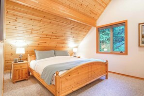 A bedroom with a wooden ceiling, a bed with a wooden frame, two bedside tables with lamps, and a window with a view of trees. - Wildwood Snowline Cabin Near Mt Baker (Deming)