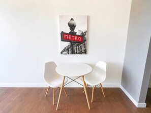 Una habitación con una mesa blanca y dos sillas blancas, un cuadro colgado en la pared y suelo de madera.