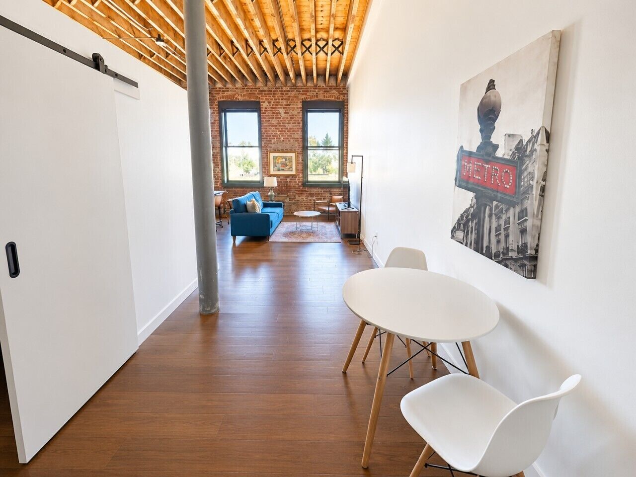 Un interior moderno con techo de madera, un comedor con mesa y sillas blancas, y una sala de estar con sofá azul.