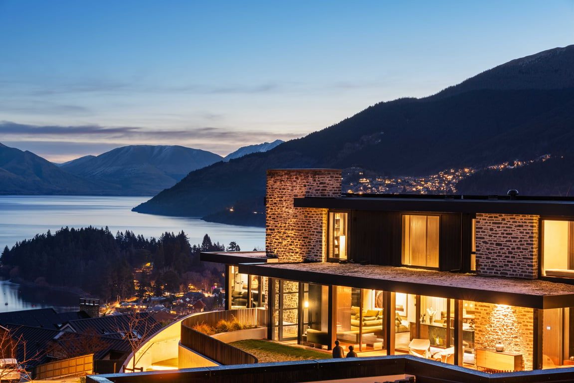A modern building with a glass facade, a brick exterior, and a view of a lake and mountains.