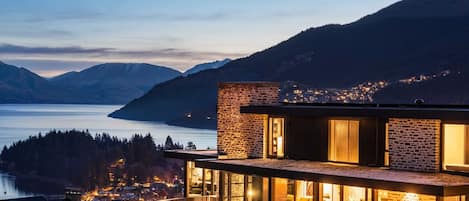 A modern building with a glass facade, a brick exterior, and a view of a lake and mountains.