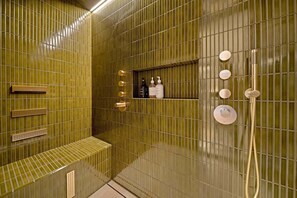 Een badkamer met een groene betegelde muur, een bankje, een plank met toiletartikelen en een douchegedeelte.