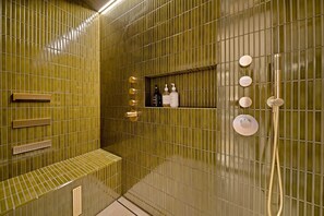 A bathroom with a green tiled wall, a bench, a shelf with toiletries, and a shower area. - Wakatipu Heights by Sotheby's Luxury Rental Homes (Queenstown)