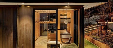 A modern house with a glass door leading to a bedroom with a bed, a chair, and a small table.