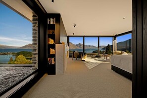 A bedroom with a large window, a bookshelf, a bed, and a view of mountains and water. - Wakatipu Heights by Sotheby's Luxury Rental Homes (Queenstown)