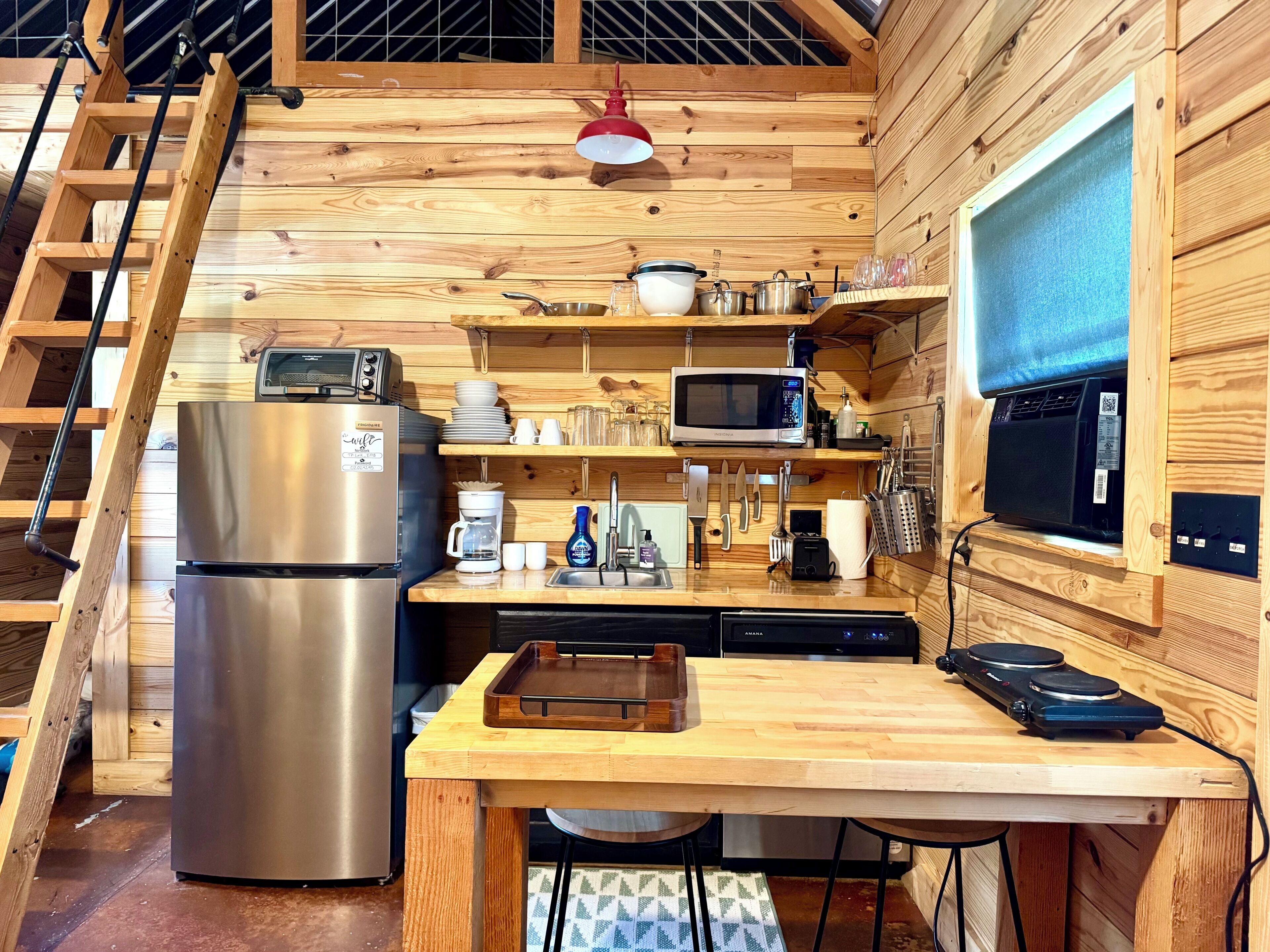 A compact kitchen with wooden walls, a stainless steel refrigerator, a microwave, and a coffee maker.