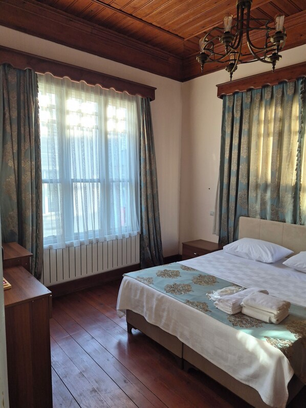 A bedroom with a bed, a nightstand, a wooden floor, a radiator, and a chandelier.