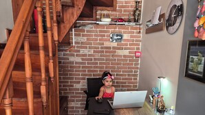 Una habitación con pared de ladrillo, una escalera de madera, un escritorio con una computadora portátil y una zona de recepción.