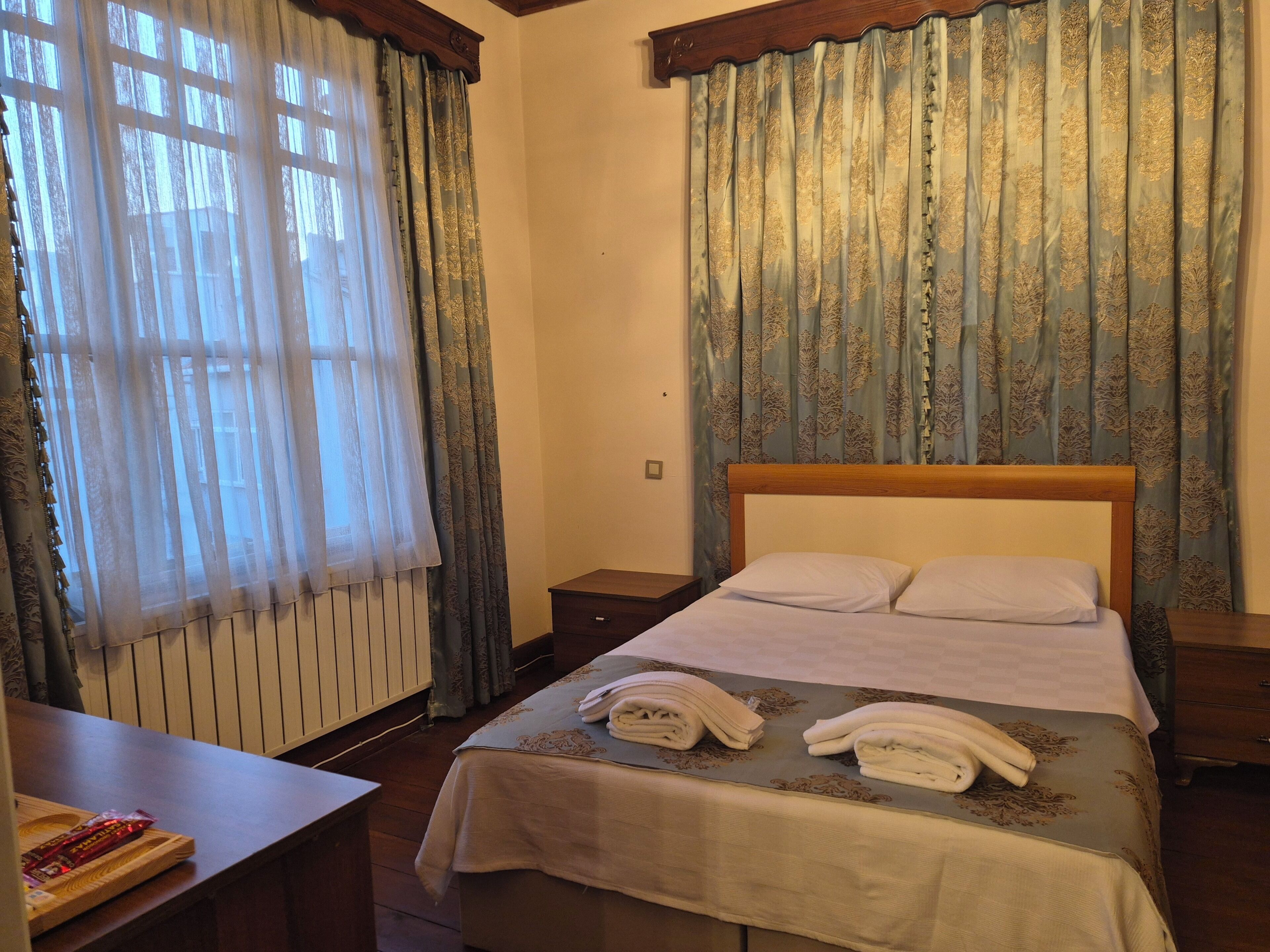 Una habitación de hotel con cama, mesita de noche, escritorio y ventana con cortinas.