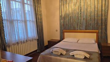 Una habitación de hotel con cama, mesita de noche, escritorio y ventana con cortinas.