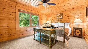 Un dormitorio de cabaña de madera con cama, escritorio, lámpara y ventilador de techo.
