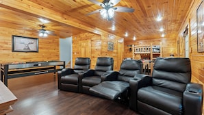 Un interior de madera con mesa de billar, sillones reclinables y ventiladores de techo.
