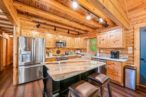 A modern kitchen with wooden cabinetry, stainless steel appliances, and a granite countertop. - MtnView Luxury Cabin with Game Room, Hot Tub, and Theater (Gatlinburg)