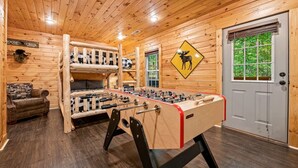 Una habitación acogedora con mesa de fútbol de mesa, literas y una puerta con señal de advertencia sobre fauna silvestre.