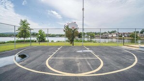 An outdoor basketball court with a net, surrounded by a chain-link fence, near a body of water and buildings. - Gorgeous 2-bedroom condo with beautiful pool, hot tub, and more in Hot Springs (Hot Springs)