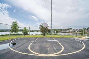 An outdoor basketball court with a net, surrounded by a chain-link fence, near a body of water and buildings. - Gorgeous 2-bedroom condo with beautiful pool, hot tub, and more in Hot Springs (Hot Springs)