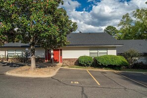 A building with a red door, a parking lot, and a tree in front. - Gorgeous 2-bedroom condo with beautiful pool, hot tub, and more in Hot Springs (Hot Springs)