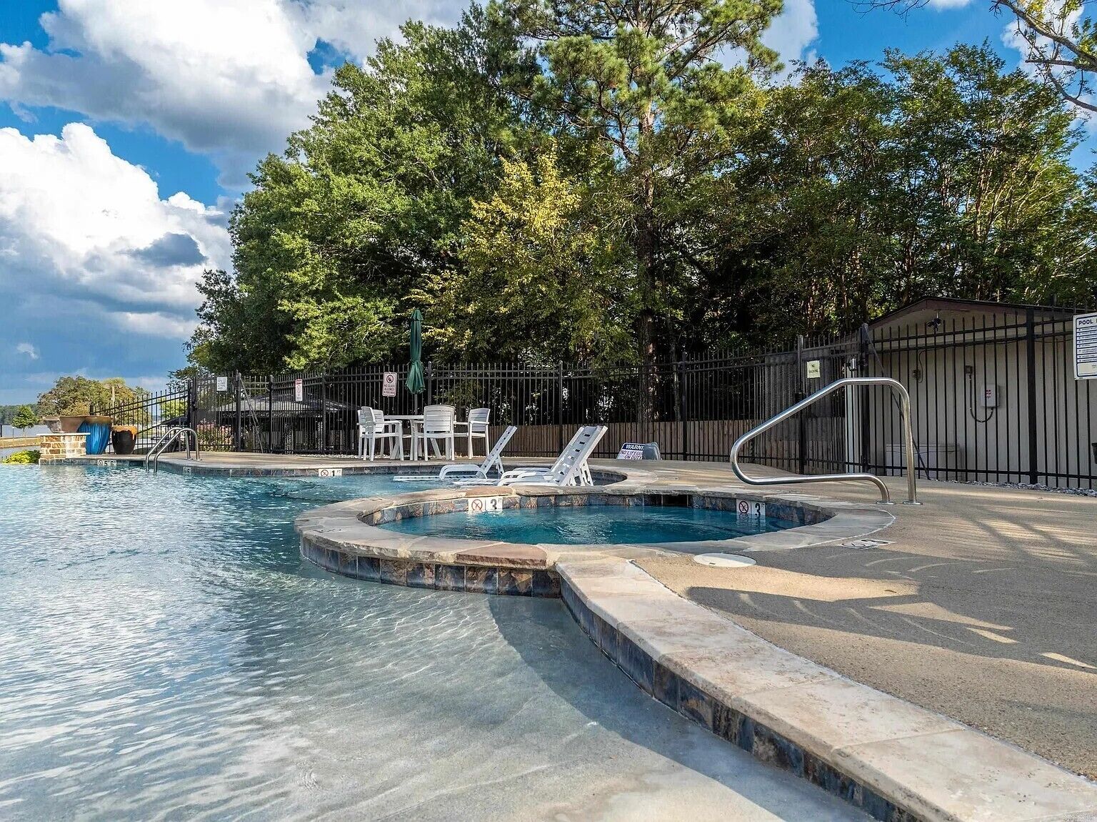 A swimming pool with a hot tub, lounge chairs, and a fenced area with tables and chairs.