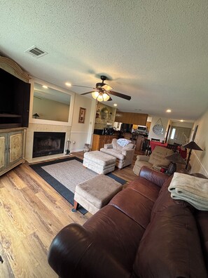 A living room with a fireplace, a ceiling fan, and a kitchen in the background. - Gorgeous 2-bedroom condo with beautiful pool, hot tub, and more in Hot Springs (Hot Springs)