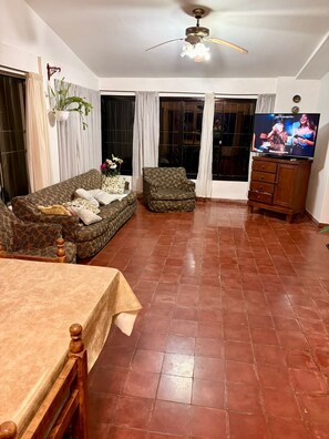 Ein Wohnzimmer mit Sofa, Sessel, Fernseher und Esstisch.